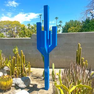 Vista sculpture resembling a geometric cactus in bold blue steel, displayed in a desert garden.