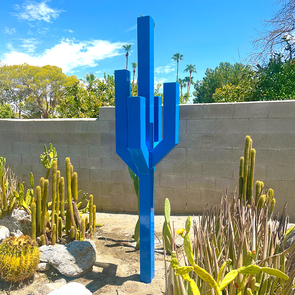Vista sculpture resembling a geometric cactus in bold blue steel, displayed in a desert garden.