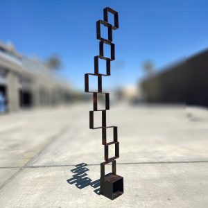 Equilibrium sculpture featuring stacked steel squares with a rust patina finish, balanced vertically outdoors.