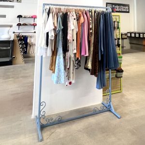 Custom metal clothing rack with decorative scroll details, painted light blue, holding assorted garments in a retail store.