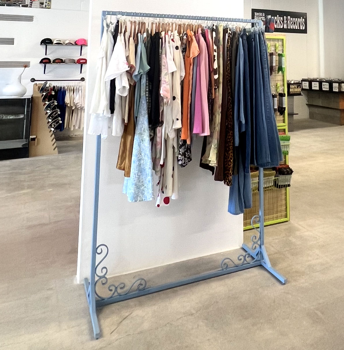 Custom metal clothing rack with decorative scroll details, painted light blue, holding assorted garments in a retail store.