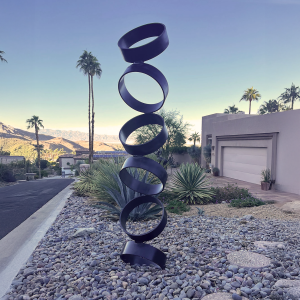 Cascade sculpture by Atomic Metalworks, featuring stacked steel rings balanced vertically in a modern desert landscape.