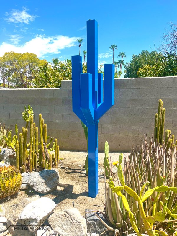 A tall steel sculpture in bright blue, resembling a cactus with arms extending outward at 45 degrees and turning upward at another 45 degrees, creating a modern, angular design.