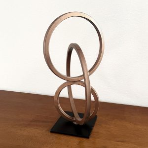 Nexus sculpture featuring interlocking bronze steel rings on a black base, displayed on a wood surface.