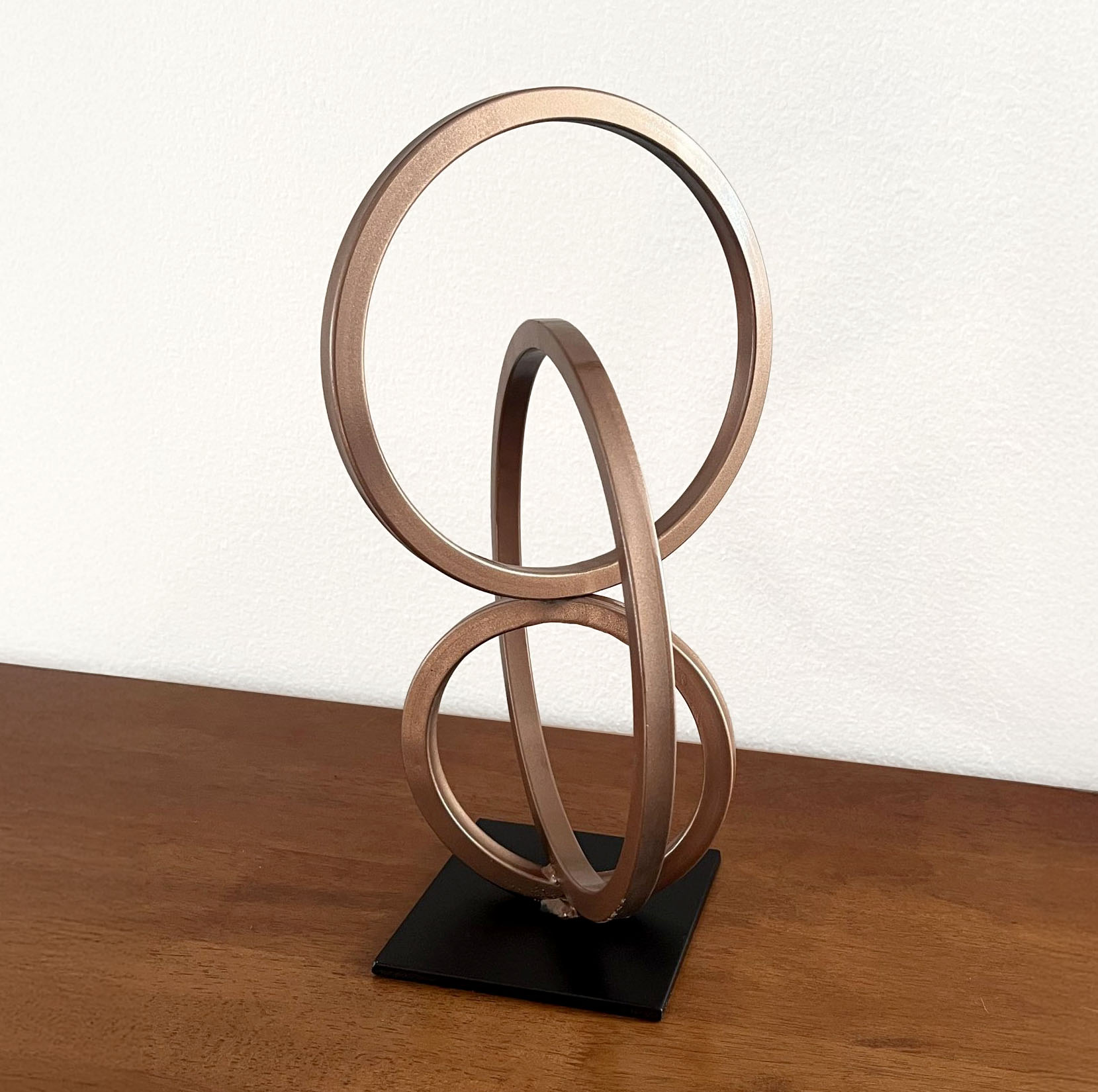 Nexus sculpture featuring interlocking bronze steel rings on a black base, displayed on a wood surface.