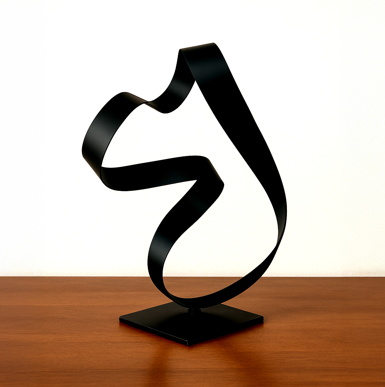 Arcus sculpture featuring a flowing black steel ribbon form on a square base, displayed on a wood surface.